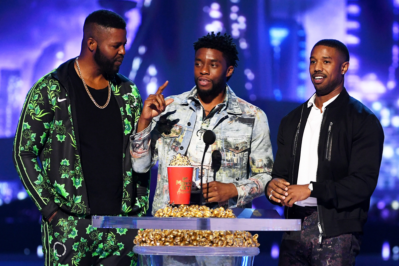 (L-R) Black Panther actors Winston Duke (wearing a tracksuit from Nike’s Nigeria World Cup Kit), Chadwick Boseman, and Michael B. Jordan accept the Best Movie award for ‘Black Panther’ onstage during the 2018 MTV Movie And TV Awards on June 16, 2018.
